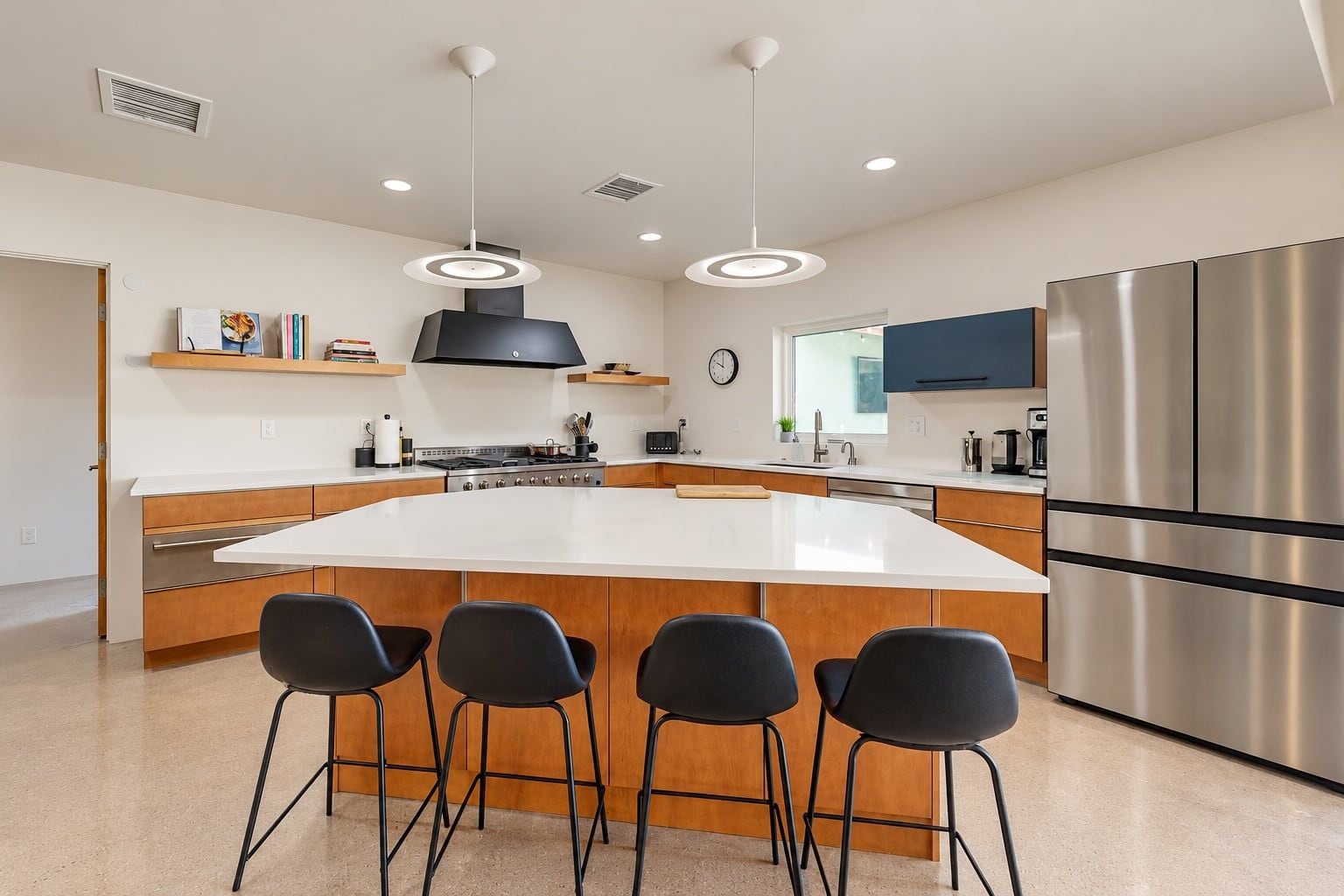 A modern kitchen with a large island, stainless steel appliances, and black bar stools.
