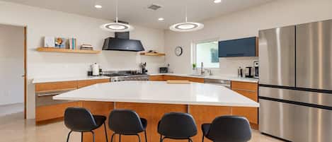 A modern kitchen with a large island, stainless steel appliances, and black bar stools.