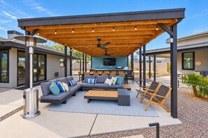 An outdoor patio with a covered seating area, a barbecue grill, and a modern house in the background.