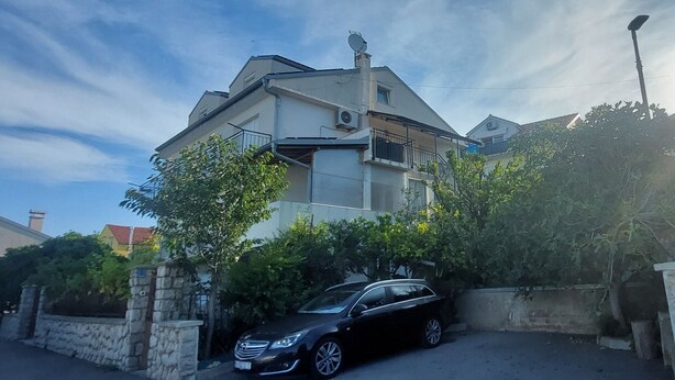 Una casa de dos pisos con un balcón, un coche aparcado y un muro de piedra.