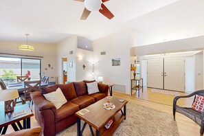 A living room with a brown leather sofa, wooden coffee table, and a dining area with a table and chairs. - Mountain-view home with shaded patio, large yard, on-site golf & tennis (Tucson)