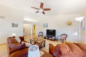 Una sala de estar con ventilador de techo, televisor, dos sillones, un sofá y una lámpara.