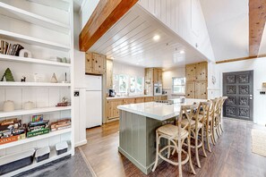 A spacious kitchen with wooden cabinets, a central island, and a dining area with bar stools. - Dog-friendly, renovated home with fireplace & amazing deck (Idyllwild)