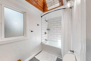 Un baño con una bañera blanca, una ventana y una ducha.