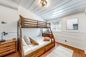 Una cama litera con una escalera, una mesita de noche con lámpara y un espejo en la pared.