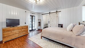 A bedroom with a wooden dresser, a bed with a beige bedspread, a television on the dresser, and a sliding barn door.