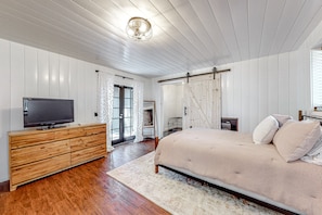 A bedroom with a wooden dresser, a bed with a beige bedspread, a television on the dresser, and a sliding barn door. - Dog-friendly, renovated home with fireplace & amazing deck (Idyllwild)