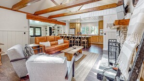 A spacious living room with a high ceiling, exposed wooden beams, a leather sofa, a wooden coffee table, and a fireplace.