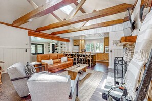 A spacious living room with a high ceiling, exposed wooden beams, a leather sofa, a wooden coffee table, and a fireplace.