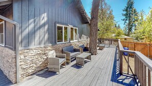 A wooden deck with wicker furniture, a stone wall, and a large tree.