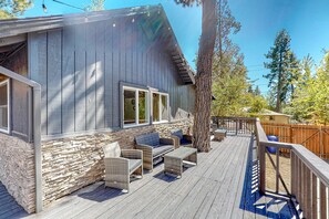 A wooden deck with wicker furniture, a stone wall, and a large tree.