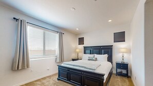 A bedroom with a large bed, two bedside tables with lamps, a window with curtains, and a carpeted floor. - Modern 55+ home with community pool, clubhouse, gym, pickleball (Goodyear)