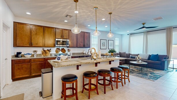 A modern kitchen with wooden cabinets, a central island with stools, and pendant lighting. - Modern 55+ home with community pool, clubhouse, gym, pickleball (Goodyear)