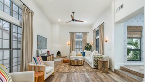 A spacious living room with a high ceiling, large windows, and a ceiling fan. There are multiple seating areas with sofas and a coffee table. - Designer dream home with opulent backyard, private pool, hot tub, game room & AC (Scottsdale)