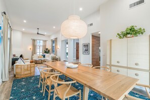 Un comedor espacioso con una larga mesa de madera, sillas de mimbre y una lámpara colgante.