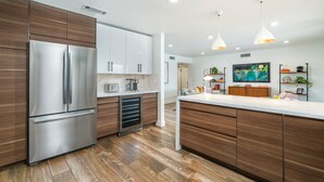 A modern kitchen with a stainless steel refrigerator, wooden cabinets, and a central island. - Designer dream home with opulent backyard, private pool, hot tub, game room & AC (Scottsdale)
