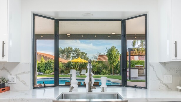 A modern kitchen with a large window overlooking a swimming pool and outdoor seating area. - Designer dream home with opulent backyard, private pool, hot tub, game room & AC (Scottsdale)