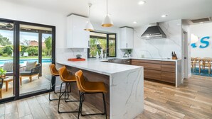 A modern kitchen with a large island, bar stools, and a view of the outdoor pool. - Designer dream home with opulent backyard, private pool, hot tub, game room & AC (Scottsdale)