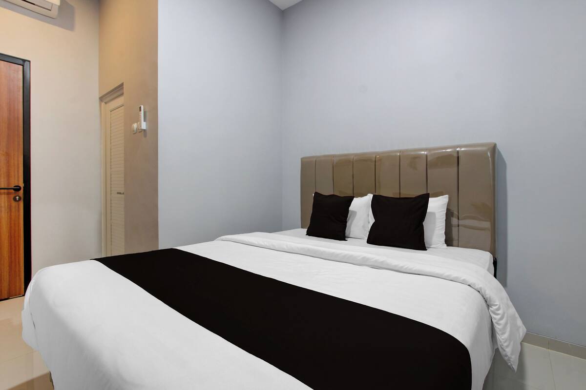 Een hotelkamer met een bed, een deur en een lichtschakelaar aan de muur.