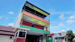 Un immeuble à plusieurs étages, doté d’une façade verte et rouge, d’un balcon à l’étage supérieur et d’une entrée couverte.