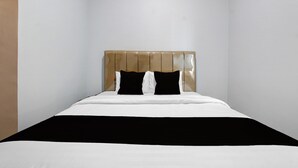 Un lit avec une tête de lit, deux oreillers noirs et un couvre-lit blanc.