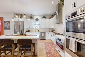 A modern kitchen with white cabinets, a central island with chairs, a Bosch oven, and pendant lighting. - Updated luxury home with ensuite bedrooms, fireplace, & large deck w/ firepit (Flagstaff)