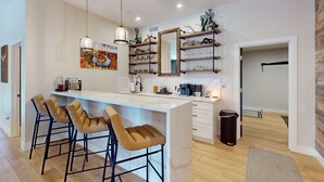 A modern kitchen with a central island, bar stools, pendant lighting, and decorative shelves. - Updated luxury home with ensuite bedrooms, fireplace, & large deck w/ firepit (Flagstaff)