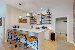 A modern kitchen with a central island, bar stools, pendant lighting, and decorative shelves. - Updated luxury home with ensuite bedrooms, fireplace, & large deck w/ firepit (Flagstaff)