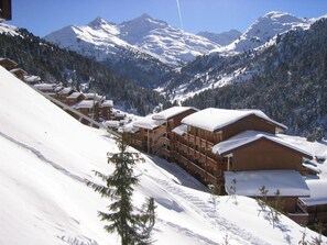 Een bergresort met een laag sneeuw, houten chalets en een piste.