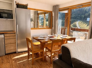 A compact kitchen with a refrigerator, wooden dining table, and chairs. - 130m from ski slopes, 9th floor, view ski slopes, balcony, ski locker, 73m², Méribel-Mottaret (Méribel - Les Allues)