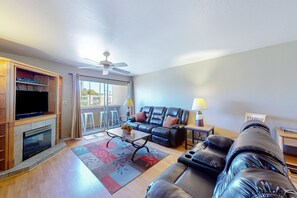A living room with a fireplace, a leather sofa, a television, and a ceiling fan. - Welcome to this luxurious condo in Scottsdale with mountain views (Scottsdale)