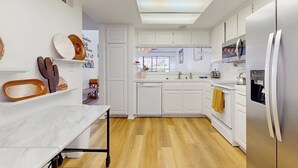 A modern kitchen with white cabinets, a marble countertop, and a wooden floor. - Bright and cheery home close to Coachella with pool & tennis on-site (Palm Desert)