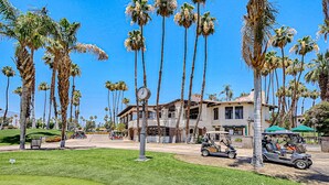 A large house with a spacious lawn, surrounded by tall palm trees. - Bright and cheery home close to Coachella with pool & tennis on-site (Palm Desert)