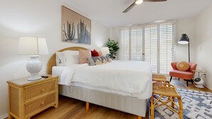 A bedroom with a bed, bedside table, nightstand, ceiling fan, window with blinds, and a chair. - Bright and cheery home close to Coachella with pool & tennis on-site (Palm Desert)