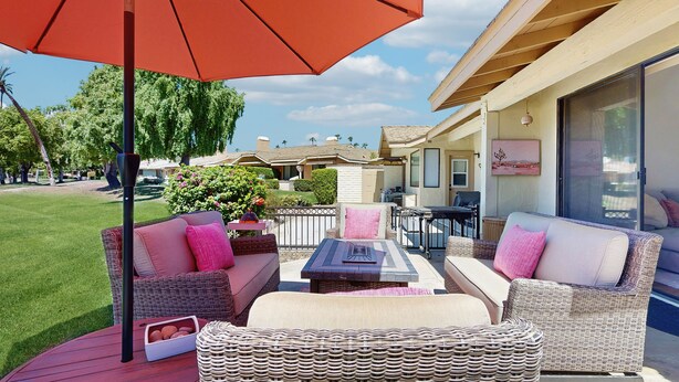 A patio area with wicker furniture, a table, and a red umbrella. - Bright and cheery home close to Coachella with pool & tennis on-site (Palm Desert)