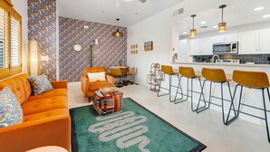 A modern living room with a sofa, chairs, and a coffee table. There is a kitchen area with a microwave and bar stools. - Vibrant, dog-friendly escape on bike path with washer/dryer, AC, pool, & hot tub (Tucson)