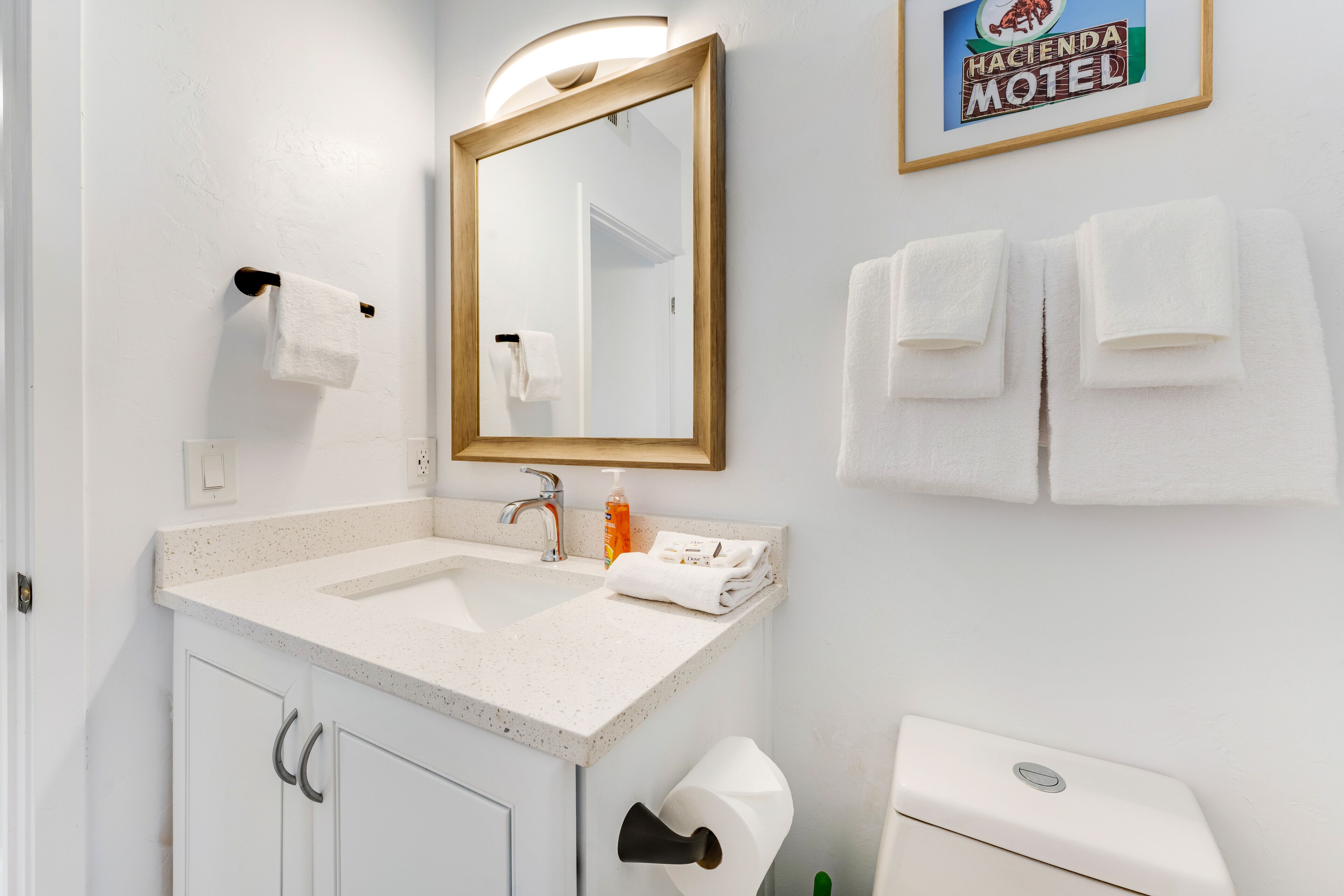 Une salle de bain avec un lavabo blanc, un miroir, des toilettes et deux serviettes accrochées au mur.