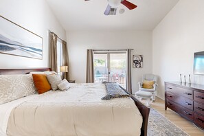 Ein geräumiges Schlafzimmer mit einem großen Bett, einem Deckenventilator, einem Fernseher, einem Sessel und Blick ins Freie.
