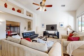 Ein geräumiges Wohnzimmer mit großem Flachbildfernseher, bequemen Sofas, einem Couchtisch und einem Deckenventilator.