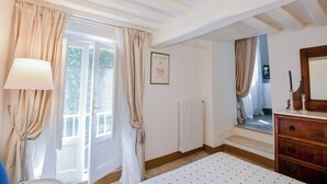 Une chambre à coucher avec un lit, une commode, un radiateur et une fenêtre avec des rideaux.