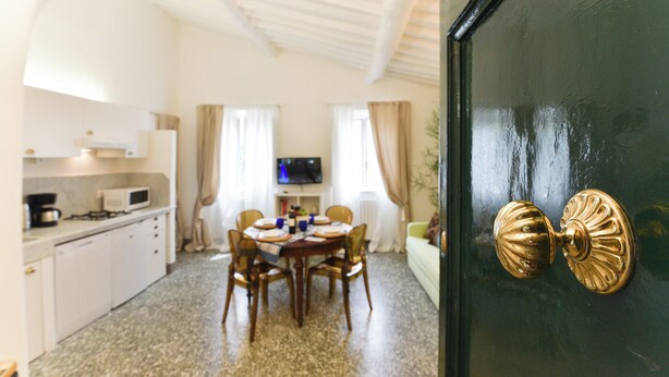 Un coin repas avec une table dressée pour quatre personnes, une cuisine avec des meubles blancs et un téléviseur fixé au mur.