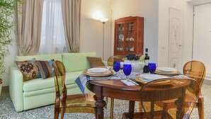Un coin repas avec une table en bois dressée pour quatre personnes, un canapé vert et un meuble avec des portes en verre.
