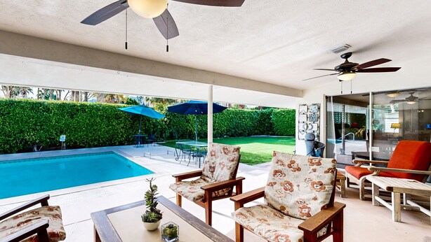 A covered patio area with a pool, outdoor furniture, ceiling fans, and a view of a green lawn. - Eclectic  mid-century, dog-friendly home with private pool, yard & gas grill (Palm Springs)