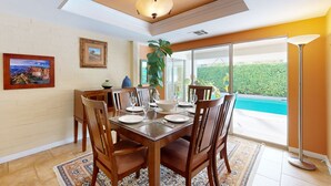 A dining area with a table set for four, a large window with a view of a pool, and a ceiling fan. - Eclectic  mid-century, dog-friendly home with private pool, yard & gas grill (Palm Springs)