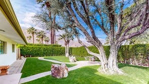 A well-maintained garden with a large tree, a stone pathway, and a patio area with outdoor furniture. - Eclectic  mid-century, dog-friendly home with private pool, yard & gas grill (Palm Springs)