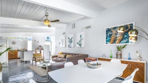 Een moderne woonkamer met een eethoek, met een witte tafel, witte stoelen, een bruine bank en een plafondventilator.