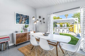 A modern dining area with a white table, white chairs, and a wooden cabinet. - Iconic, bright, & dog-friendly house w/private pool, spa, pool table & grill (Palm Springs)