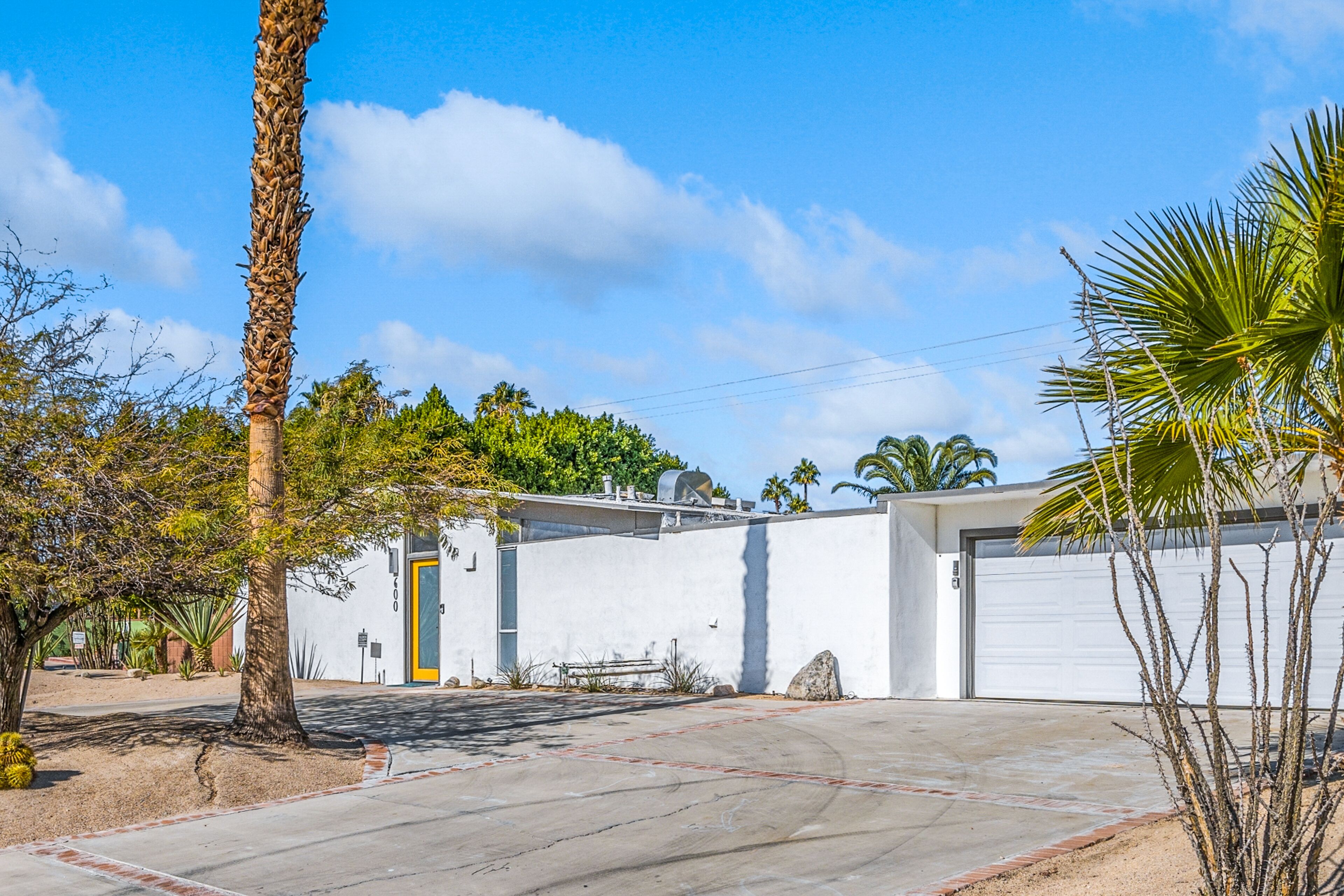 A white building with a garage door, surrounded by palm trees and a clear blue sky.