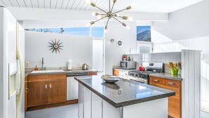 Een moderne keuken met een centraal eiland, houten kastjes, een roestvrijstalen kookplaat en een bijzondere wandklok.