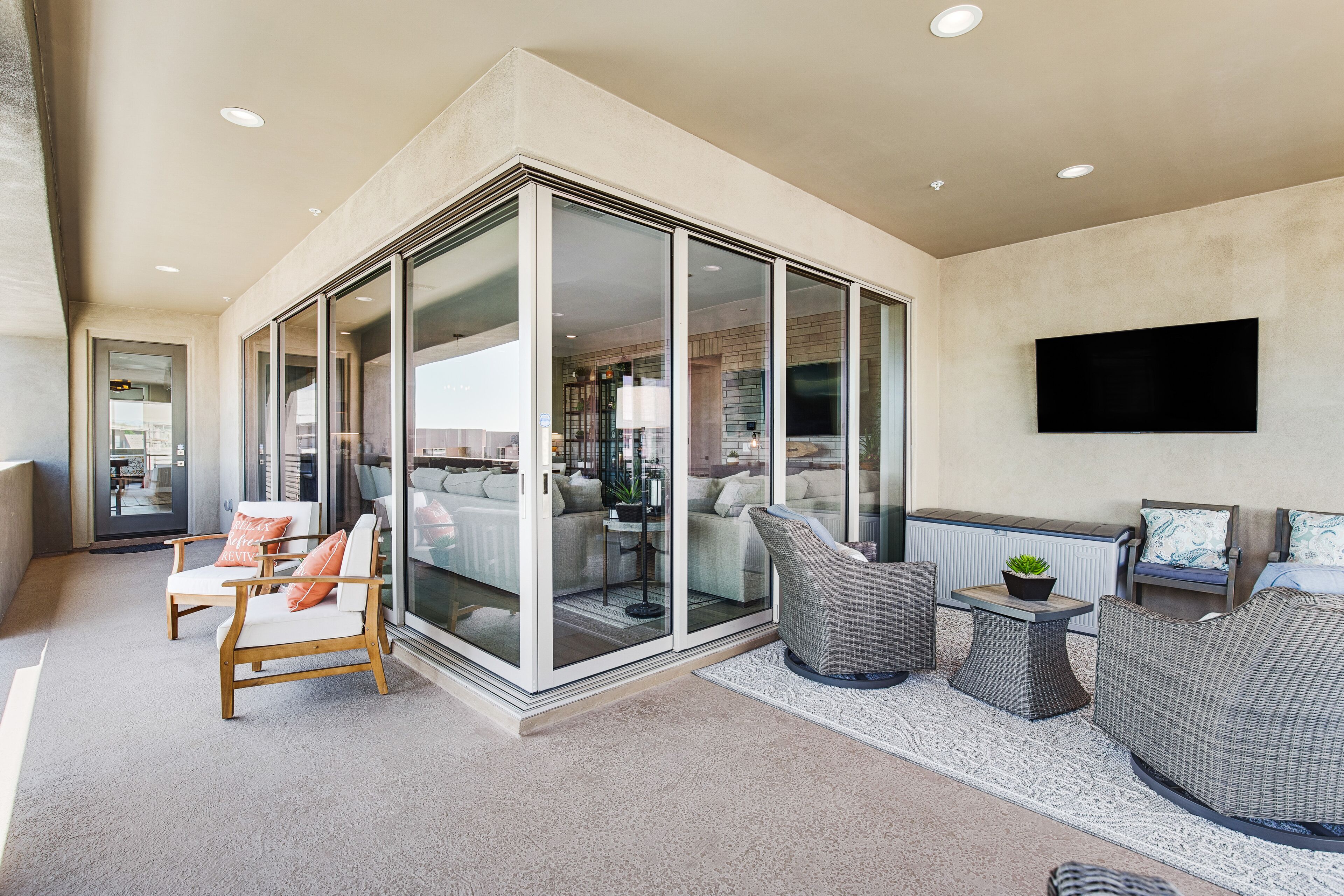 A modern living room with a glass partition, comfortable seating, a flat-screen TV, and a small side table with a plant.